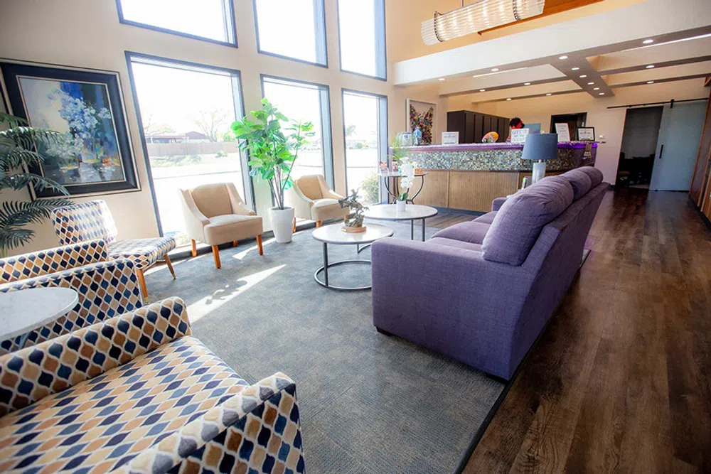 Bright modern lobby with tall windows, patterned chairs, purple sofa, and wooden reception desk in the background