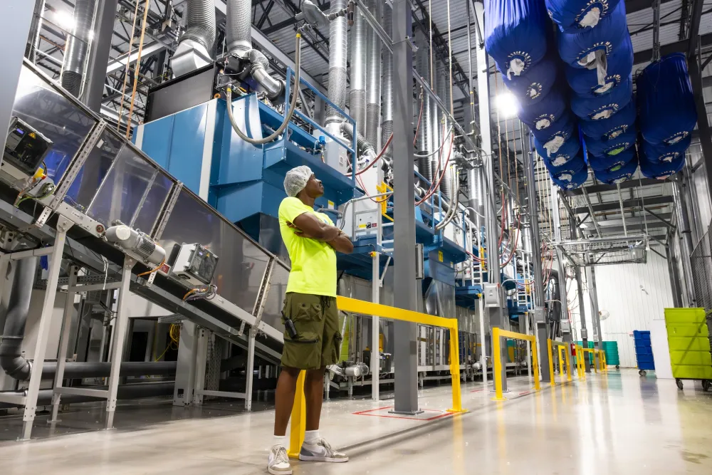 Worker in safety gear inspects large industrial machinery inside a bright, clean manufacturing facility.