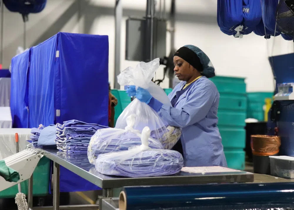 Worker packaging clean laundry in clear plastic bags in an industrial laundry facility with blue textiles