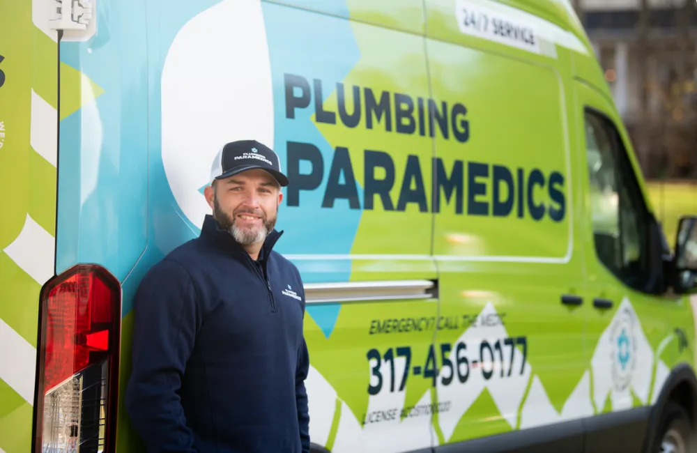 A plumbing technician stands beside a bright green service van with 'Plumbing Paramedics' branding.