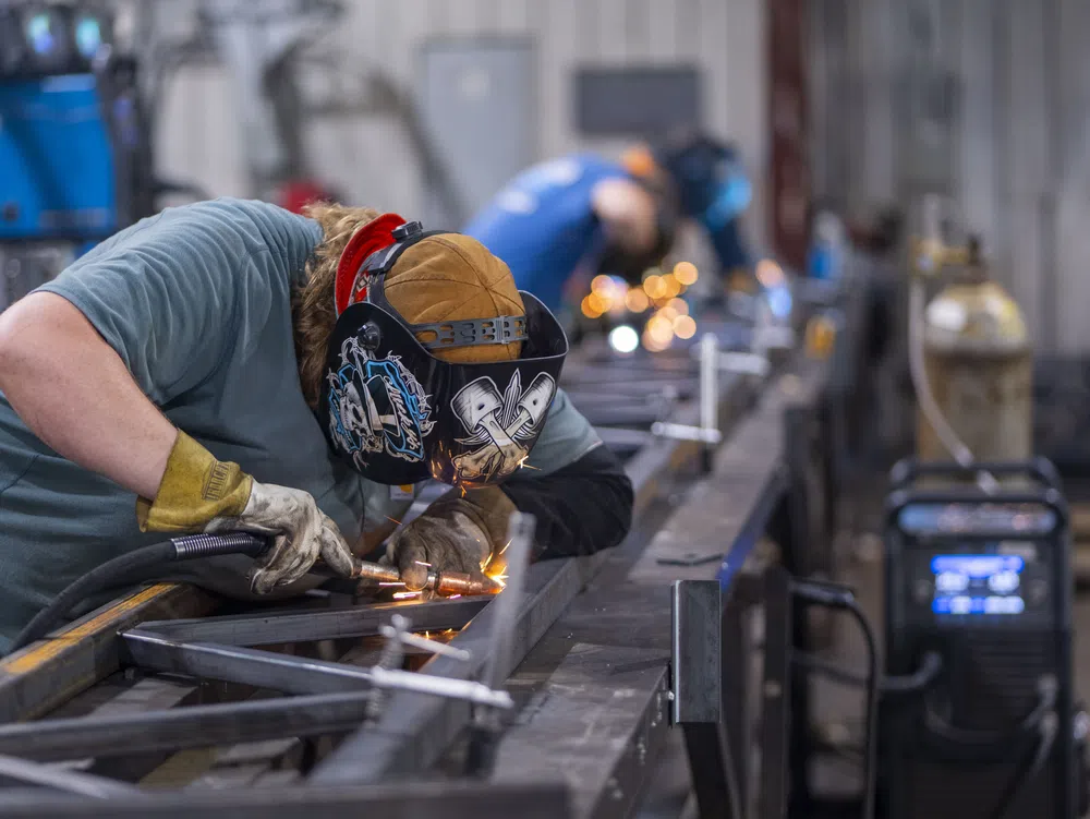 Welder wearing protective gear welding metal framework with sparks in an industrial workshop.