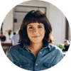 Smiling woman with short dark hair wearing denim shirt in a bright, modern indoor setting.