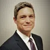 Professional man in a suit and tie smiling with a neutral background in a corporate headshot photo.