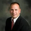 Professional businessman in suit and red tie smiling against a dark blurred background.