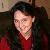 Smiling woman with long dark hair wearing a red top sitting on a couch indoors.