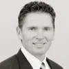 Black and white headshot of a man in a suit smiling against a plain background