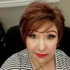 Woman with short auburn hair, red lipstick, striped shirt, and subtle makeup in an indoor setting