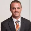 Professional man wearing a dark suit and patterned tie smiling against a plain background