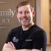 Smiling male dentist in black scrubs standing with arms crossed at Heritage Family Dentistry office.