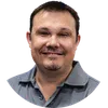 Smiling man with short dark hair and goatee wearing a gray collared shirt against a white background
