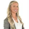 Professional woman with long blonde hair in business attire smiling against a white background.