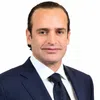 Professional businessman in navy suit with white shirt and textured tie against plain white background