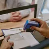 Hand stamping an approved mark on documents with a blue rubber stamp at a service counter.