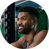 Smiling man with beard and curly hair lifting weights in a gym with green weight plates in background