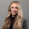 Professional headshot of a smiling woman with long blonde hair wearing a gray blazer and black top