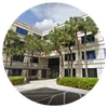 Modern office building with palm trees and clear blue sky surrounding the parking area entrance.