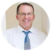 Smiling middle-aged man wearing glasses and a blue striped tie in a light-colored shirt against a neutral background