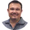 Smiling man with short dark hair and goatee wearing a blue collared shirt against white background