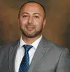Professional man in gray suit and blue polka dot tie smiling against a brown background
