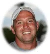 Smiling man wearing a white baseball cap and gray shirt with blurred outdoor background