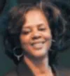 Smiling woman with curly hair and hoop earrings in a dark blurred background
