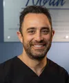 Smiling male dentist in black scrubs with North Oaks Dental logo and name tag standing indoors.