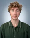 Portrait of young man with tousled blonde hair wearing a textured green polo shirt against a gradient blue background