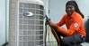 Technician in Estes Services uniform smiling while servicing a Carrier air conditioning unit with tools and gauges.