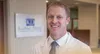 Smiling male dentist in white coat standing in dental office with Kiechner Dental sign in background
