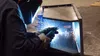 Welder wearing protective gear welding metal with sparks flying in a workshop environment.