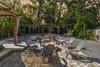 Outdoor backyard patio with fire pit surrounded by six chairs and string lights overhead at sunset.