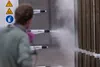 Person operating spray guns applying coating to metal panels in an industrial setting