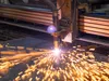 Industrial plasma cutting machine producing bright sparks while cutting metal sheet on factory floor