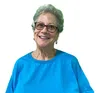 Smiling elderly woman wearing glasses and a bright blue t-shirt against a white background.