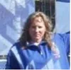 Smiling woman in blue jacket outdoors with long curly hair and a blurred background.