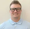Smiling young man with short spiked hair and black glasses wearing a light blue polo shirt.