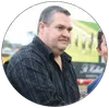 Man in black striped shirt standing outdoors with blurred green and yellow background in circular frame