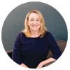 Smiling blonde woman in navy blue top sitting on a chair against a gray background