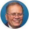 Smiling elderly man with glasses in a suit against a blue circular background