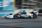 White and black open-wheel racecar with Mobil 1 branding speeding on racetrack with blurred spectators in background.