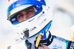 Close-up of a race car driver wearing a blue and white Bell helmet with Honda and CarIQ Pay logos, adjusting his suit.