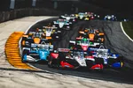 Multiple IndyCar race cars closely competing on a curved track during a high-speed race.