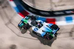 IndyCar racing car with blue and white livery speeding on a curved track with red, white, and blue curbs.