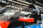 Close-up of a race car cockpit with driver wearing helmet inside, featuring sponsors and overlaid text reading OPLiGHT.