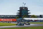 Indy cars racing on track near grandstand and scoring pylon at Indianapolis Motor Speedway