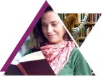 Woman in a pink scarf reading a book with another woman reaching for a book in a library shelf.