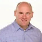 Smiling bald man in a light purple checkered shirt against a plain white background