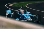 Blue IndyCar race car on a racetrack with blurred foreground and curved asphalt in the background