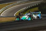 Open-wheel race car speeding on curved track with blurred background and bright sunlight