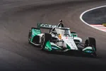 IndyCar race car with green and white livery speeding on a curved asphalt track during daytime.
